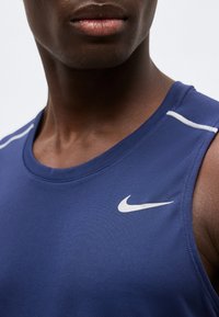 Κοντινό πλάνο ενός ατόμου που φορά γαλάζιο αθλητικό αμάνικο μπλουζάκι Nike με λευκό λογότυπο και λευκές ρίγες στους ώμους.