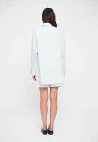 Μπλε και λευκή ριγωτή πουκαμίσα με άνοιγμα στο πίσω μέρος, συνδυασμένη με αντίστοιχες κοντές παντελόνες. Λείο ύφασμα, άνετη εφαρμογή και μακριά μανίκια.