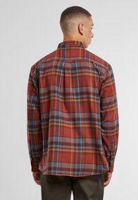 Red and gray plaid shirt with long sleeves, button cuffs, and a back yoke design. Made from a textured fabric with a relaxed fit.