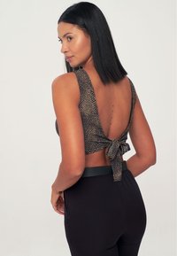 Top corto con stampa leopardata, con spalline larghe e schiena annodata, abbinato a pantaloni neri a vita alta; texture liscia e forma aderente.