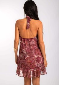 Vestido con cuello halter en una tela transparente y estampada con tonos de burdeos y rosa. Presenta un dobladillo con volantes y un detalle con lazo en la parte posterior.