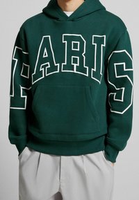 Felpa verde con cappuccio e scritta bianca "PARIS". Presenta una tasca a marsupio e polsini e orlo a costine. Realizzata in morbido materiale in pile.
