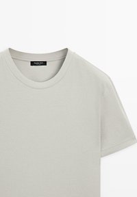 Lysegrå T-shirt med korte ærmer og rund hals, synlige sømme ved kraven og sort mærke med branding på indersiden af halsudskæringen.