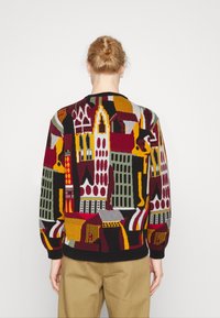 Suéter de punto con un diseño vibrante de paisaje urbano en rojo, amarillo, verde y gris, con un cuello y puños acanalados.