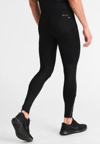Leggings de sport noirs avec un design ajusté, mettant en avant un logo Dri-FIT, des panneaux texturés et une poche zippée à l'arrière.