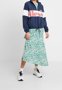 Marinblå och vit zip-up tröja med röd logga, kombinerad med en grön blommig midi-kjol och vita sneakers, med sidofickor.