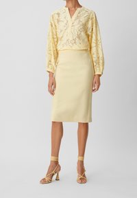 Gul spetsblus med långa ärmar över en enfärgad gul pennkjol. Strapiga gula klackar med ankelsnörningar fulländar outfiten.