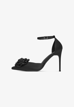 Melnas satīna augstpapēžu kurpes ar norādītu purngalu, ziedu akcentu priekšā, plānu potītes siksniņu un mirdzošu stiletu papēdi.