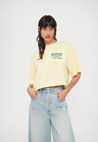 T-shirt jaune court avec texte vert imprimé sur le devant, accompagné d'un jean large bleu clair avec poches avant et détails usés.