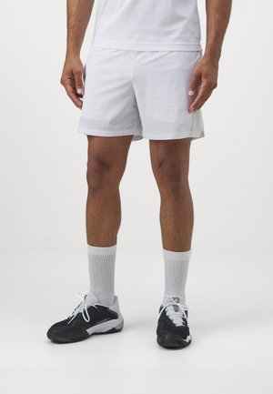 Witte sportshorts van lichtgewicht materiaal, met een subtiele logo, gecombineerd met zwarte sportschoenen en witte korte sokken.