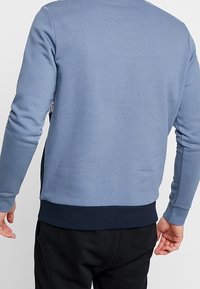 Světle modrá mikina s žebrovaným tmavě modrým lemem. Vyrobena z měkkého materiálu s dlouhými rukávy, s jednoduchým designem bez viditelných grafik.