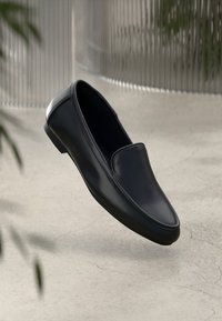 Black leather slip-on shoe with a rounded toe and minimalistic design. Smooth texture and low-profile rubber sole. Lightweight and streamlined.