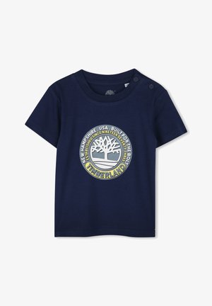 T-shirt in cotone blu navy con maniche corte, caratterizzato da un logo circolare Timberland in giallo e grigio, e bottoni a pressione sulla spalla.