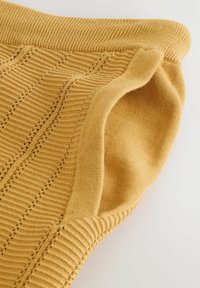 Manche de pull en tricot jaune moutarde avec revers côtelé et motifs verticaux texturés sur un fond clair.