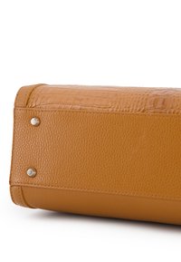 Fond d'un sac à main en cuir tan avec des textures en cuir grainé et crocodile, mettant en avant deux clous en métal et des coutures renforcées sur un fond blanc.