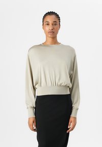 Beige gekürztes Langarmoberteil mit gerafftem Saum, glatter Textur, Rundhalsausschnitt und elastischen Bündchen, kombiniert mit einem schwarzen Rock.