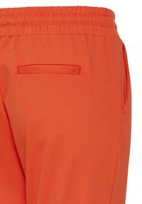 Pantalones deportivos naranjas con cintura elástica, que cuentan con un solo bolsillo trasero y una tela suave y texturizada.