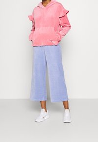 Sudadera de terciopelo rosa con mangas con volante, bolsillo delantero y detalle de corazón. Pantalones cortos de pana azul clara con pierna ancha. Zapatillas blancas.