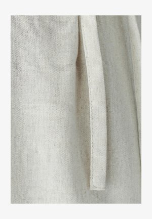 Hele beež kangas tekstuurse kudumisega, millel on lame rihma detail. Materjal on tõenäoliselt linane või puuvillane, näidates loomulikku viimistlust.