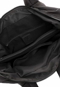 Interno di una borsa nera in tessuto con due tasche con zip, una texture morbida e una piccola etichetta in pelle vicino al centro.
