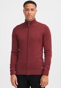 Maglione zip-up bordeaux con colletto e polsini a coste; realizzato in materiale a maglia; presenta un piccolo etichetta del marchio vicino all'orlo.