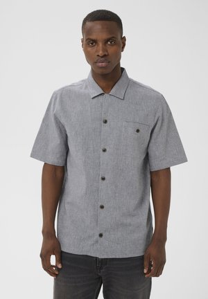 Man draagt een grijs, kort mouwtjes overhemd met structuur en een borstzak, staand tegen een effen lichte achtergrond.