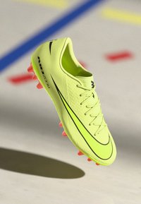 Botín de fútbol amarillo neón con parte superior texturizada, acentos negros, seis tacos rosas y un diseño aerodinámico para un rendimiento mejorado.