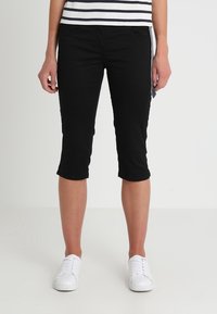 Svarta capribyxor i stretchmaterial, med slim fit, medelhög midja och knälång längd. I kombination med vita sneakers.