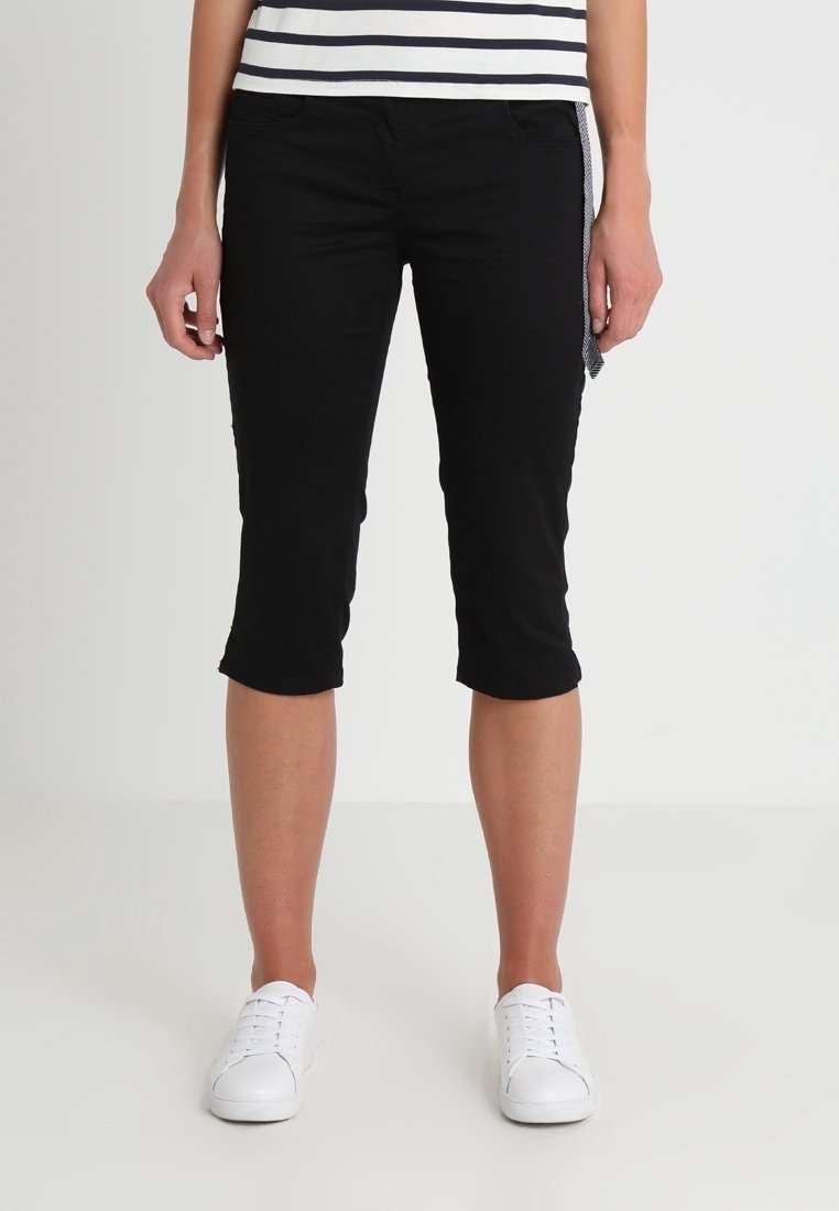 Svarta capribyxor i stretchmaterial, med slim fit, medelhög midja och knälång längd. I kombination med vita sneakers.