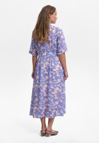 Robe midi florale en tissu léger et transparent avec un motif de feuilles roses et bleues, manches courtes et taille ceinturée.
