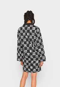 Vestido de padrão preto e branco com um formato oversized, mangas longas e designs abstratos sobre um fundo quadriculado.