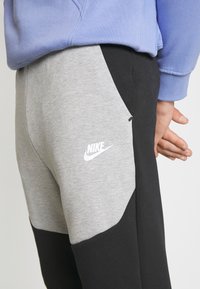 Grå och svarta Nike-mjukisbyxor med sidoficka. Har en vit Nike-logotyp på den grå delen. Mjuk textur, sportig design.