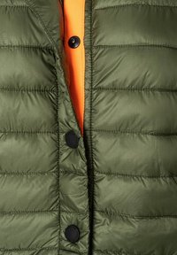 Gepolsterte Weste in Olivgrün mit horizontalen Nähten, ausgestattet mit schwarzen Druckknöpfen und einer leuchtend orangefarbenen Innenauskleidung. Weiche Textur und leichtes Design.