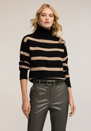 Schwarz-beige gestreifter Rollkragenpullover aus weichem Material, mit lockerem Schnitt und gerippten Bündchen, kombiniert mit olivgrünen Hosen und einem Nieten-Gürtel.