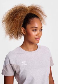 Lys grå t-shirt med korte ærmer. Har et logo på brystet og kontrastfarvede beige detaljer på skuldrene. Behageligt bomuldsblandingsmateriale.