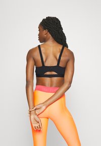 Črna športna modrčka z nastavljivimi naramnicami, z izrezom na hrbtu. V kombinaciji z živahnimi oranžnimi leggins ali pa s pink pasom.