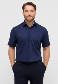 Camicia a maniche corte di colore blu navy, realizzata in tessuto liscio, con una tasca sul petto e dettagli a righe sotto il colletto.