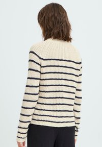 Krämfärgad stickad tröja med marinblå horisontella ränder, texturerad tyg, ribbade ärmslut och rund hals, sedd bakifrån.