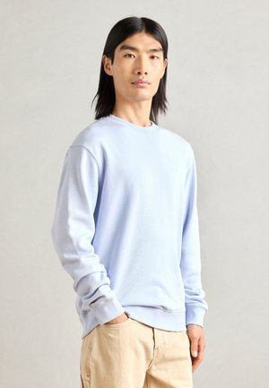 Light blue sweatshirt in soft fabric, featuring a round neckline and ribbed cuffs. Notable detail: small square logo on the chest.