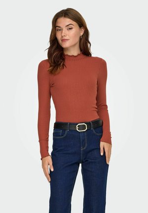 Rustfarvet ribbet langærmet top med bølget halsudskæring, parret med mørkeblå jeans og et sort bælte med en sølvspænde.