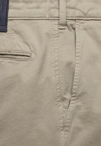 Khaki broek van een gladde katoenen stof, met een knoopsluiting, schuine zijzakken en een geweven label op de tailleband.