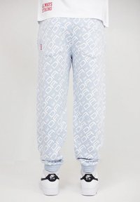 Light blue joggers with a repeating white logo pattern, featuring elastic cuffs and back pockets, paired with white sneakers.