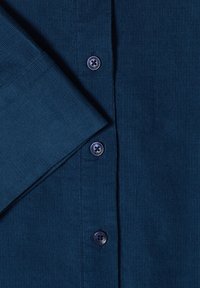 Tissu côtelé bleu foncé avec des boutons assortis et une manche repliée, montrant une fine texture tricotée verticale sur un vêtement.