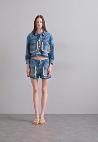 Denim cropped takki kahdella suurella taskudella ja yhteensopivat shortsit, joissa on kuluneet reunat ja koristeelliset ommeltu yksityiskohdat.