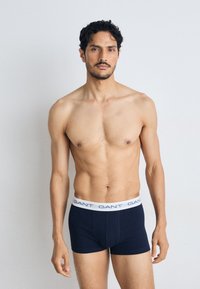 Tumesin navy boxers valge vöökohta, millel on "GANT" logo. Valmistatud pehmest materjalist, omavad kehakujulist disaini ja siledat tekstuuri.