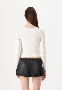 Vit ribbad tröja med långa ärmar, med en rosa halsringning. Kombinerad med en kort, mörk denimkjol med veckad design.