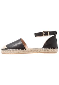 Espadrille de cuero negro con punta redonda, suela de cuerda de yute y correa en el tobillo con hebilla en tono dorado. Textura suave, diseño plano.