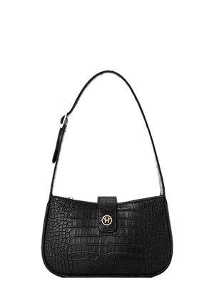 Kobieta ubrana w czarny krótki top i białe spodnie niesie na zewnątrz teksturowaną czarną torebkę na ramię ze złotym zapięciem.