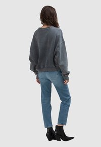 Przewymiarowana szara bluza z opuszczonymi ramionami, zestawiona z jasnoniebieskimi dżinsami i czarnymi botkami na obcasie. Gładka faktura tkaniny.