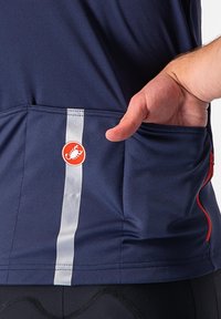 Dunkelblaues Radtrikot mit einem reflektierenden weißen Streifen, Netzstruktur und einem roten runden Logo. Verfügt über eine Seitentasche, auf der eine Hand ruht.